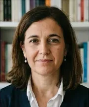 Mujer con cabello castaño oscuro, fondo de estantería con libros. Expresión seria.