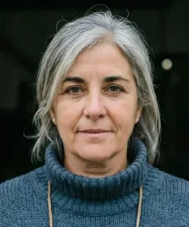Mujer de cabello canoso con suéter azul, mirando a la cámara con expresión seria.